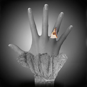 May include: A black and white photograph of a hand wearing a ring with a large, triangular, white stone with orange and purple accents. The hand is wearing a white lace cuff.