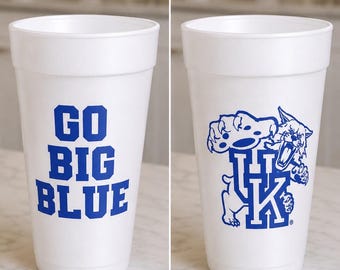 Può includere: Un bicchiere in polistirolo bianco con testo blu che recita GO BIG BLUE su un lato e una grafica blu di una mascotte gatto selvatico sopra le lettere UK sull'altro. Il bicchiere ha una forma cilindrica affusolata con un bordo liscio.