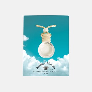 May include: A clear glass aromatherapy bottle with a wooden cap and a decorative cord, hanging against a blue sky with white clouds. The label reads "Archaic Magick" with a bee illustration and the text "Crafted Luminaries of Wax and Wick."
