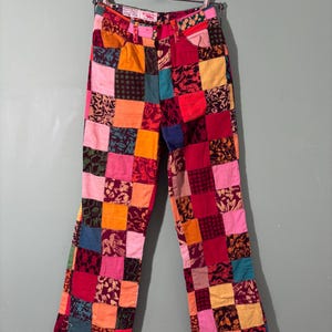 May include: Patchwork pants in a variety of colors, including red, pink, orange, yellow, green, and blue. The pants are made of fabric squares sewn together in a patchwork design. The pants are hanging on a metal hanger.