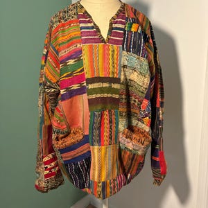 May include: A colourful patchwork shirt with a V-neck and long sleeves. The shirt is made of different fabrics with various patterns and colours, including red, green, blue, yellow, and orange.