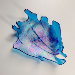 May include: A blue glass dish with an iridescent finish. The dish is shaped like a wave or a splash of water.