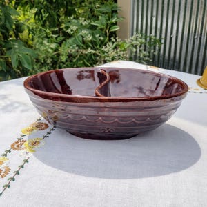 May include: A brown ceramic divided serving bowl. The bowl has a glossy finish and is divided into two sections. The exterior features a series of horizontal ridges and a decorative floral pattern. The bowl is likely vintage.