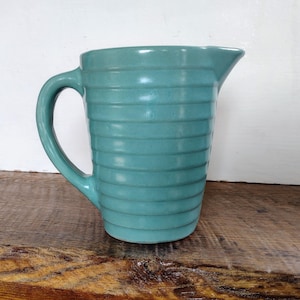 May include: A teal blue ceramic pitcher with a ribbed design. The pitcher has a handle and a spout.