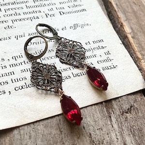 May include: A pair of earrings with a filigree design and red gemstone accents. The earrings are made of metal and have a vintage look.