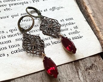 May include: A pair of earrings with a filigree design and red gemstone accents. The earrings are made of metal and have a vintage look.