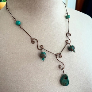 Può includere: Una collana in filo di rame con perline turchesi e marroni con motivi. La collana ha un design unico con un ciondolo pendente.