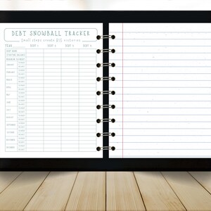 May include: A black notebook with a debt snowball tracker layout. The top of the page reads "DEBT SNOWBALL TRACKER" with the tagline "Small steps create BIG victories." The notebook has lined pages and a spiral binding.