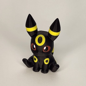 Op de afbeelding: Een 3D-geprint figuurtje van een Pokémon-personage, de evolutie van Eevee, Umbreon. Het figuurtje is zwart en geel en heeft rode ogen en een gele ring om zijn nek.