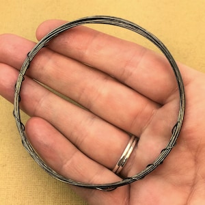May include: A close-up of a coiled wire bracelet made of thin, black and gold wire. The bracelet is held in a person's hand.