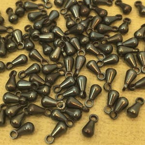 May include: A large quantity of small, teardrop-shaped metal charms with a loop at the top. The charms are a dark gunmetal color.