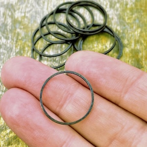 May include: A pile of 10 small, black metal rings, approximately 2.5 cm in diameter. The rings are smooth and have a slightly oxidised finish.