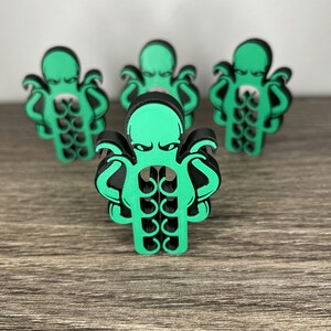 May include: Four green and black octopus-shaped figurines. The octopus has eight tentacles and a grumpy expression.
