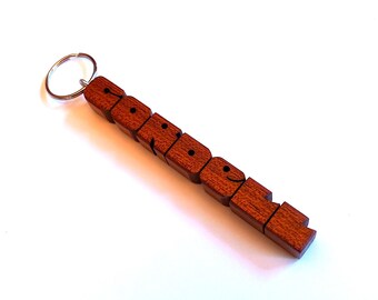 May include: A wooden keychain spelling out the word "FRIEND" in individual, connected blocks. The keychain is made of reddish-brown wood and has a silver key ring.