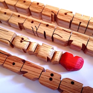 May include: Wooden articulated toy snakes with carved faces and a red painted head. The toys are made of light brown wood and are arranged in a row on a white surface. The snake's body is segmented.