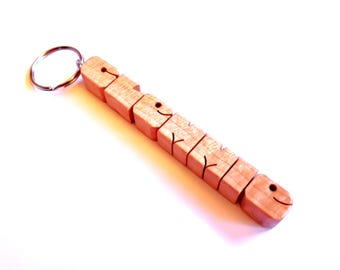 May include: A wooden keychain featuring a segmented design, resembling a caterpillar or worm. Each segment has a carved face with a smiling mouth and eye. The keychain is attached to a silver metal ring.