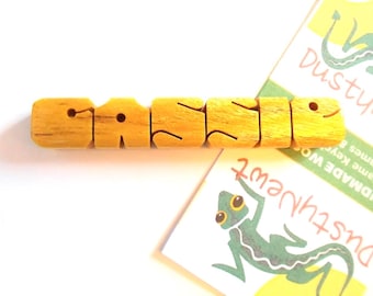 May include: Wooden name block spelling "CASSIE" in yellow. Each letter is a separate block with a rounded shape. Two cards with a green lizard illustration and the text "DustyNewt" are in the background.