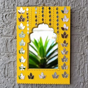 May include: A yellow mirror with a decorative archway design. The mirror is surrounded by a border of small, silver, flower-shaped tiles. The mirror is hanging on a gray wall.