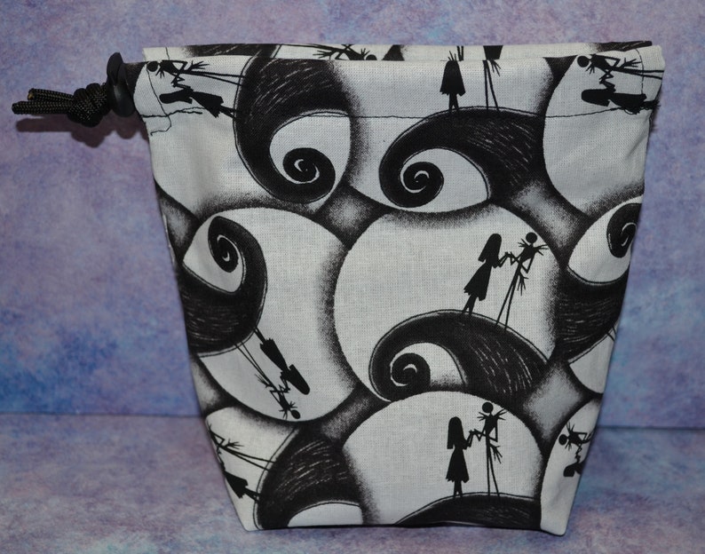 Puede incluir: Una bolsa de cord&oacute;n blanco y negro con un patr&oacute;n repetido de Jack Skellington y Sally de la pel&iacute;cula Pesadilla antes de Navidad.