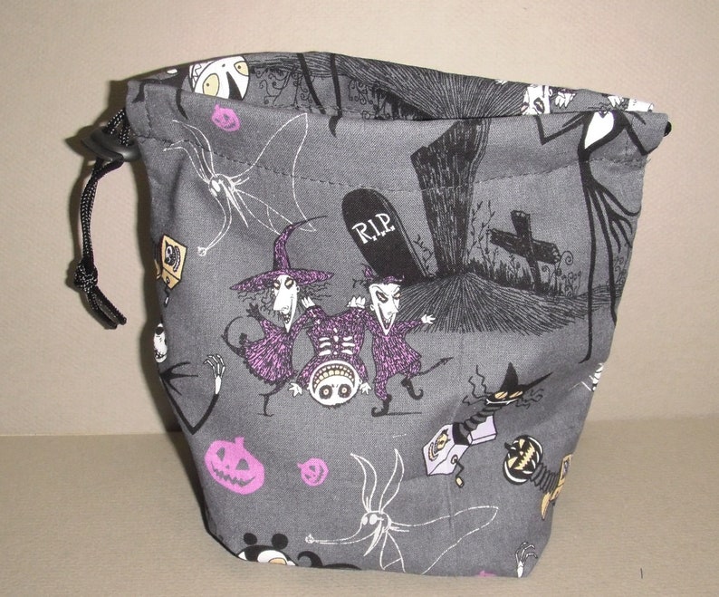 Puede incluir: Una bolsa de cord&oacute;n gris con un cord&oacute;n negro. La bolsa est&aacute; impresa con ilustraciones en blanco y negro de personajes de la pel&iacute;cula Pesadilla antes de Navidad, incluyendo a Jack Skellington, Sally y Oogie Boogie. La bolsa tambi&eacute;n tiene una l&aacute;pida con la inscripci&oacute;n "RIP".