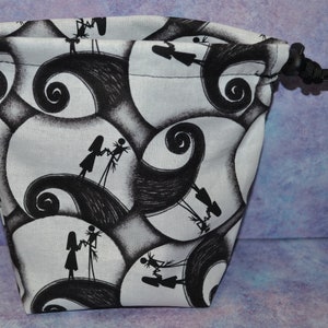 Puede incluir: Una bolsa de cord&oacute;n blanco con un estampado en blanco y negro de Jack Skellington y Sally de Pesadilla Antes de Navidad. El estampado presenta a los personajes caminando sobre un patr&oacute;n de espiral en blanco y negro.