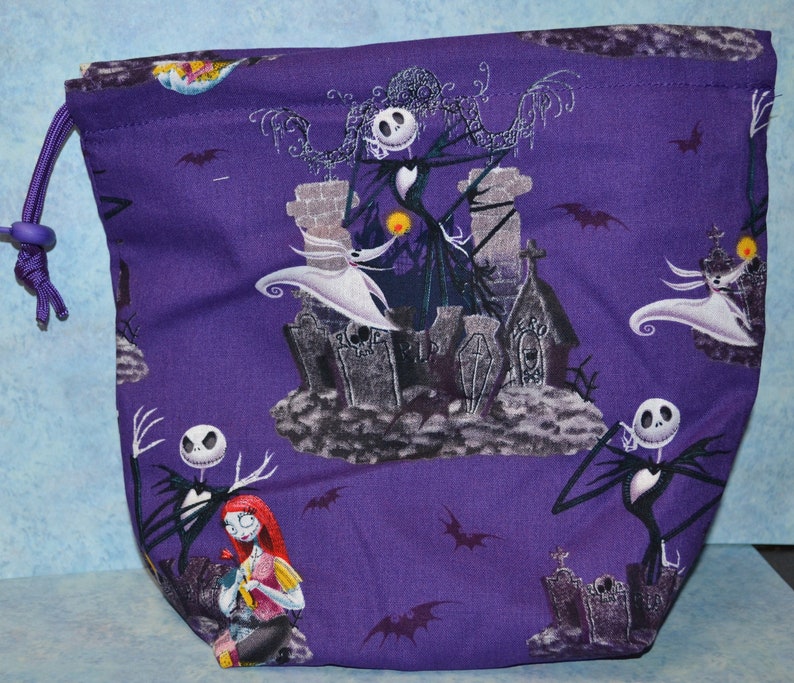 Puede incluir: Bolsa de cord&oacute;n morado con un patr&oacute;n repetido de Jack Skellington y Sally de Pesadilla Antes de Navidad. La bolsa presenta un fondo morado con ilustraciones en blanco y negro de los personajes.