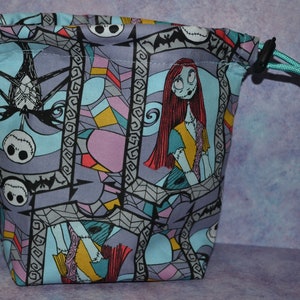 Puede incluir: Una bolsa de cord&oacute;n azul con un estampado de vitral colorido con personajes de Pesadilla antes de Navidad. El estampado incluye a Sally, Jack Skellington y murci&eacute;lagos.