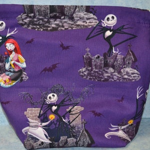 Puede incluir: Bolsa de cord&oacute;n morado con un patr&oacute;n repetido de Jack Skellington y Sally de Pesadilla Antes de Navidad. Los personajes se representan en un cementerio con murci&eacute;lagos volando en el fondo.