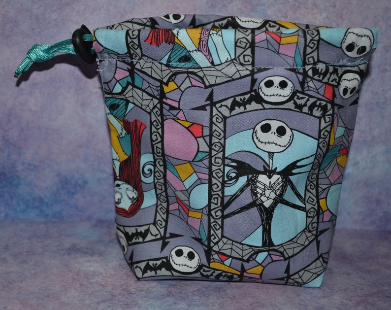 Puede incluir: Una bolsa de cord&oacute;n morado, azul y rosa con un patr&oacute;n repetido de Jack Skellington de Pesadilla antes de Navidad. La bolsa tiene un cord&oacute;n turquesa.