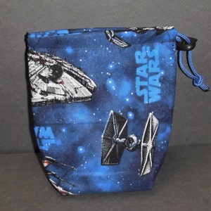 Puede incluir: Bolsa de cordón azul con temática de Star Wars. La bolsa presenta imágenes de naves espaciales de las películas de Star Wars, incluyendo el Halcón Milenario y cazas TIE. La bolsa tiene un fondo azul con estrellas blancas y el texto "Star Wars" impreso en la parte delantera.