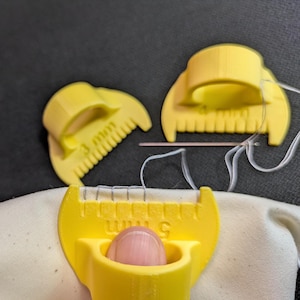 Peut inclure: Trois outils de couture en plastique jaune conçus pour espacer les points, chacun doté d'un anneau pour le doigt et d'un bord en forme de peigne. Les outils sont marqués des tailles 3 mm, 4 mm et 5 mm, et l'un est utilisé sur du tissu.