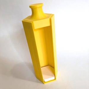 May include: A bright yellow, hexagonal-shaped vertical display stand featuring a flared top rim and a flat, white hexagonal base platform. The structure has an open front panel design, providing a clear view of the interior space and the base.