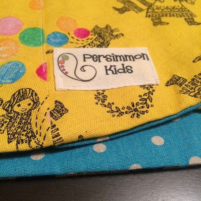 May include: Yellow fabric with a black and white design of people and animals. The fabric has a white label with the text "Persimmon Kids" in black lettering.