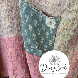 May include: Close-up of a patchwork textile with floral patterns in pink, white, and blue. A blue pocket with a white patterned design is sewn onto the fabric. The Daisy Soul Studio logo is visible.