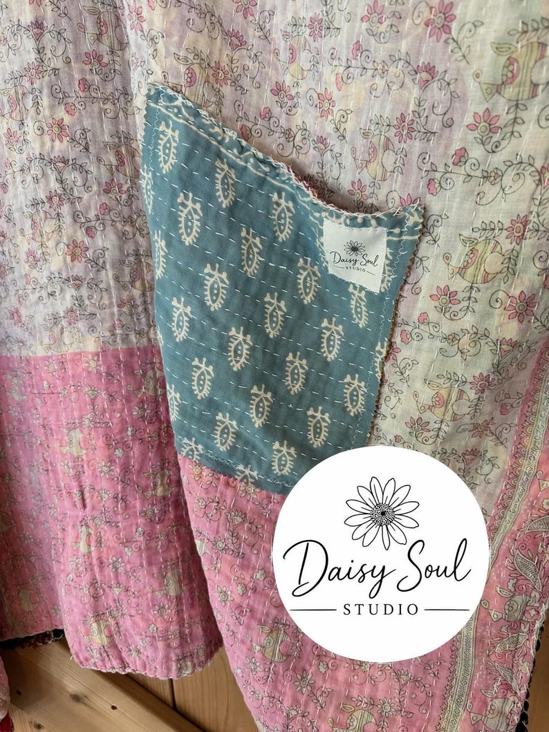 May include: Close-up of a patchwork textile with floral patterns in pink, white, and blue. A blue pocket with a white patterned design is sewn onto the fabric. The Daisy Soul Studio logo is visible.