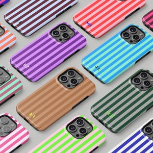 Può includere: Una collezione di custodie per telefoni colorate con motivi a righe verticali. Le custodie presentano varie combinazioni di colori, tra cui viola, marrone, verde e blu, con iniziali su alcune custodie. Le custodie sono progettate per uno smartphone.