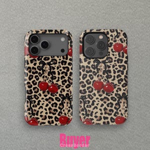 May include: Two phone cases featuring a leopard print pattern and red cherries. The cases have a black border and a glossy finish. The cherries are tied with black bows. The cases are displayed on a grey background.
