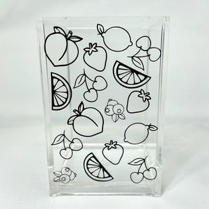 Può includere: Un contenitore trasparente in acrilico decorato con disegni a tratto nero di vari frutti, tra cui pesche, fragole, limoni, ciliegie, mirtilli e spicchi d'arancia. Il contenitore è rettangolare.