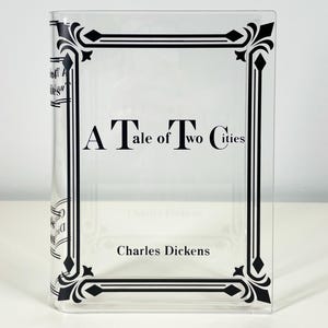 May include: A clear plastic book cover with a black and white design featuring the title "A Tale of Two Cities" by Charles Dickens.