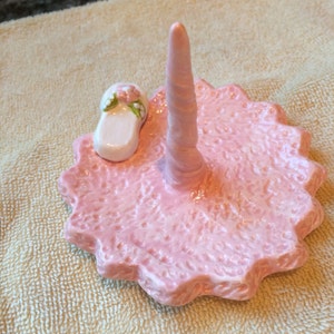 May include: Pink ceramic ring holder with a white slipper design and a single ring holder post.
