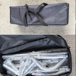 Peut inclure: Un &eacute;tui de transport noir avec une poign&eacute;e et une fermeture &eacute;clair noires. L'&eacute;tui est ouvert, r&eacute;v&eacute;lant des poteaux et des connecteurs m&eacute;talliques argent&eacute;s d&eacute;mont&eacute;s, envelopp&eacute;s dans du plastique transparent. L'&eacute;tui est sur une surface en b&eacute;ton.