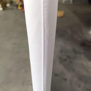 Peut inclure: Gros plan sur un tissu blanc avec une couture verticale. Le tissu pr&eacute;sente une texture subtilement c&ocirc;tel&eacute;e, et la couture est une fine ligne droite de couture. L'impression g&eacute;n&eacute;rale est propre et minimaliste.