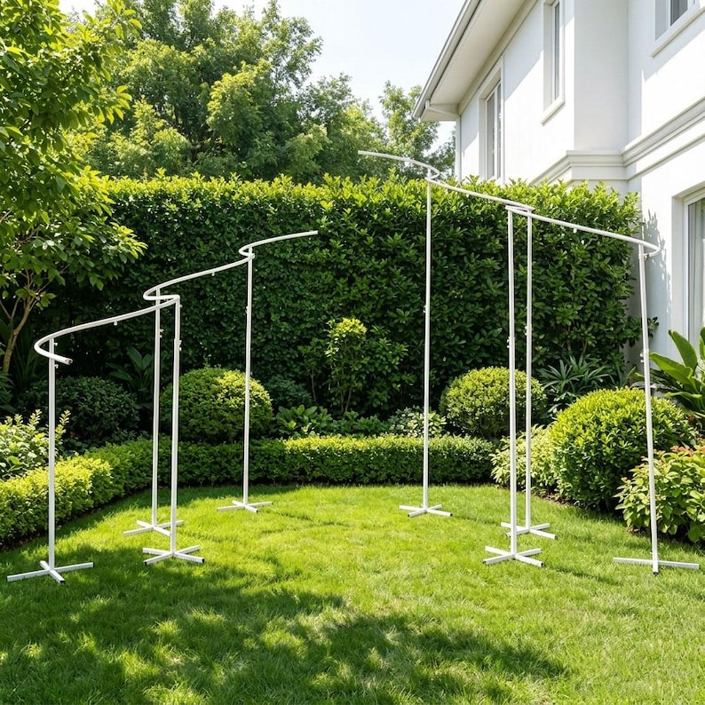 May include: A white metal backdrop stand featuring a modular design with multiple vertical poles and curved horizontal bars. The structure consists of several connected sections with cross-shaped bases, creating a tiered, wave-like frame.