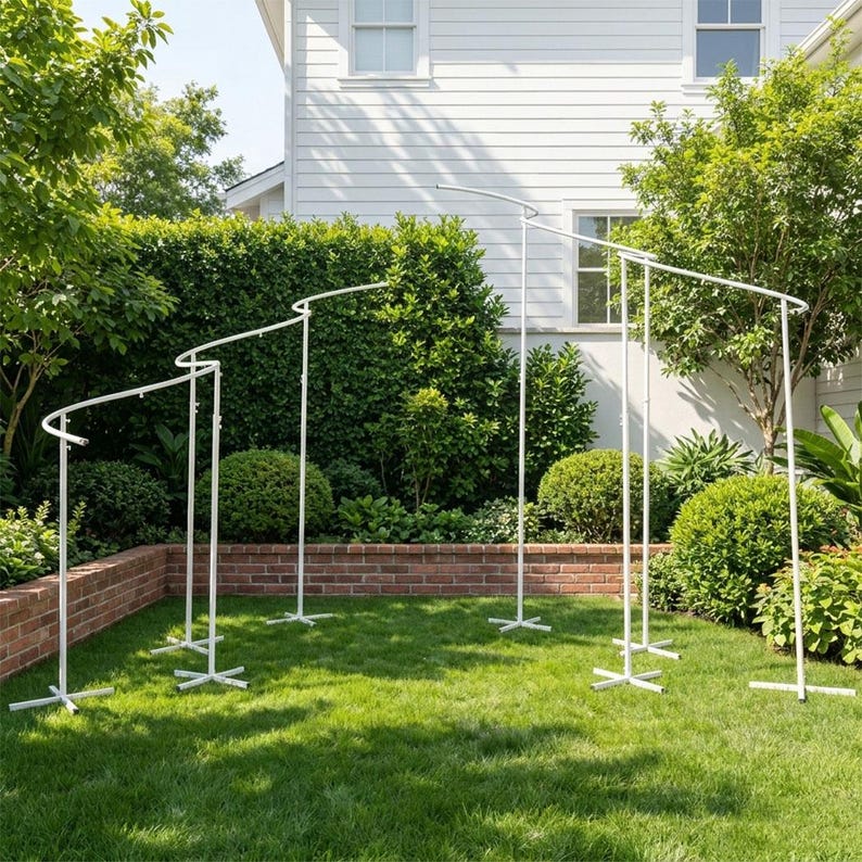 May include: A white metal arch display stand featuring a multi-tiered, cascading spiral design with four vertical poles of varying heights, each supported by a cross-shaped base, creating a continuous curved frame structure for decorative arrangements.