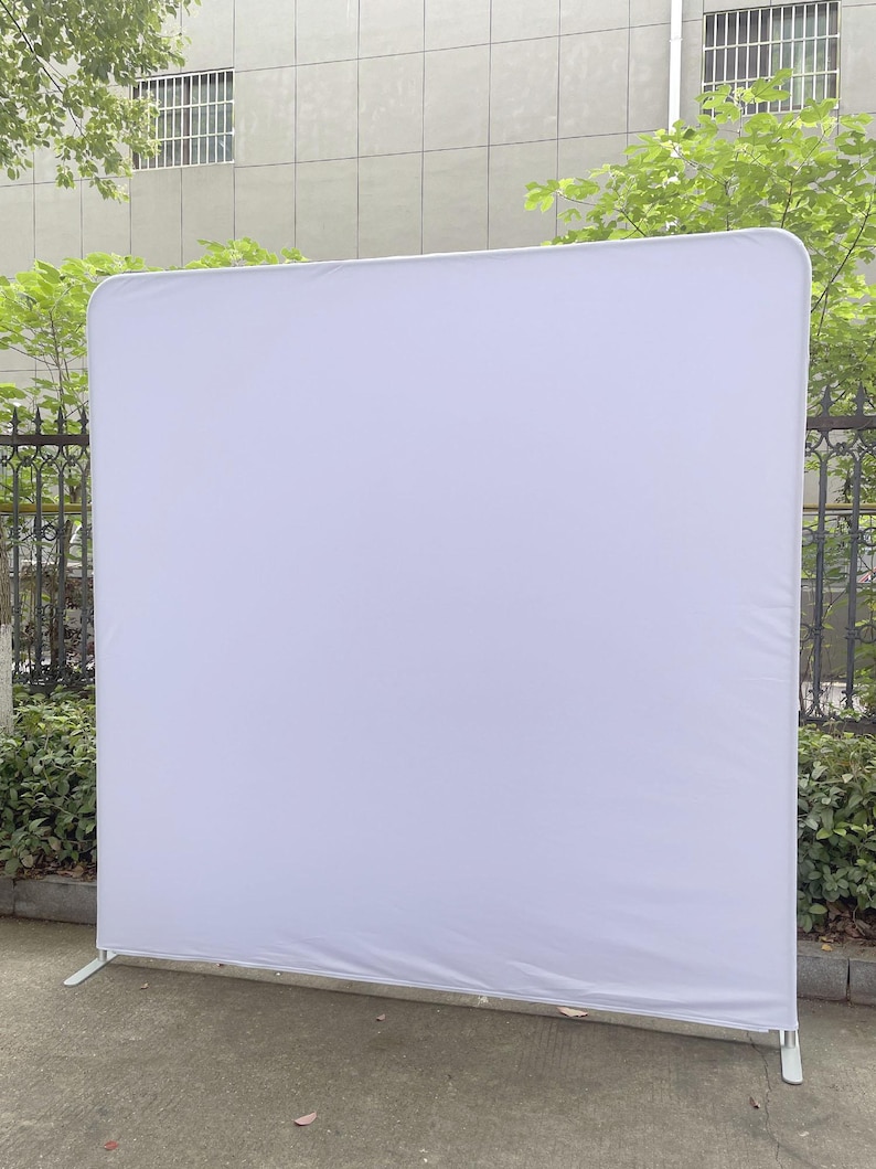 Peut inclure: Un grand &eacute;cran de fond blanc de forme rectangulaire avec des coins arrondis. L'&eacute;cran est soutenu par un cadre m&eacute;tallique blanc avec deux pieds pour la stabilit&eacute;. La toile de fond est en tissu lisse et infroissable.
