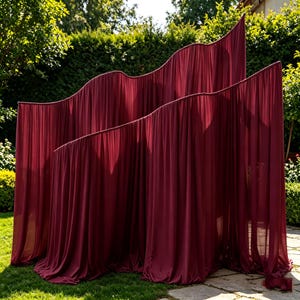 May include: A room divider featuring two tiered, wavy frames draped in deep burgundy fabric. The fabric hangs in vertical folds, creating a soft, pleated texture that follows the curved, undulating lines of the structure's top edges.