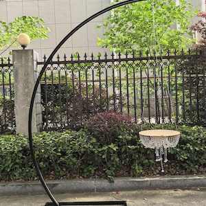 Puede incluir: Soporte de arco de metal negro con base redonda y parte superior curva. Una lámpara de araña de cristal cuelga de la parte superior del arco.