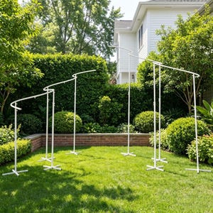 May include: A white metal arch display stand featuring a modular design with multiple vertical poles and curved top sections. The structure is composed of several connected segments supported by cross-shaped bases, creating a tiered frame.