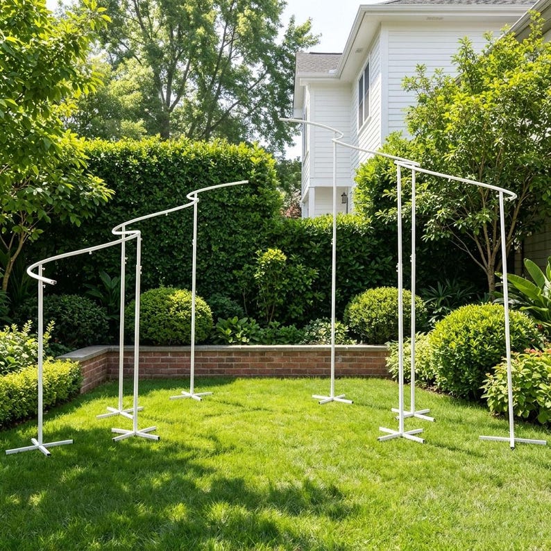 May include: A white metal arch display stand featuring a modular design with multiple vertical poles and curved top sections. The structure is composed of several connected segments supported by cross-shaped bases, creating a tiered frame.