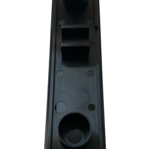 May include: Black plastic component with two round openings and a rectangular slot. The component has a textured surface and is designed for a specific purpose.